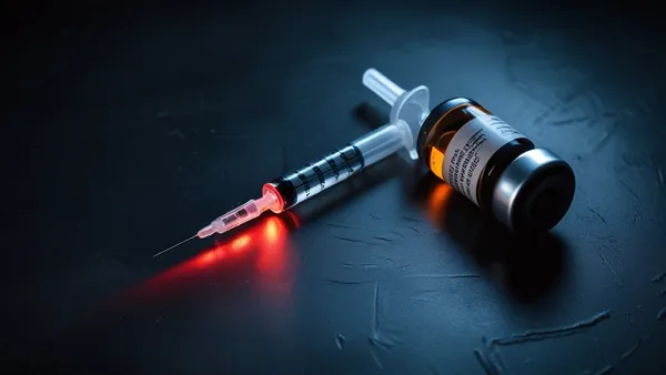 Seringa e frasco sobre superfície metálica escura com luz vermelha de alerta