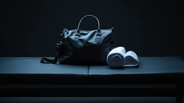 Bolsa de academia e toalha sobre banco escuro em vestiário